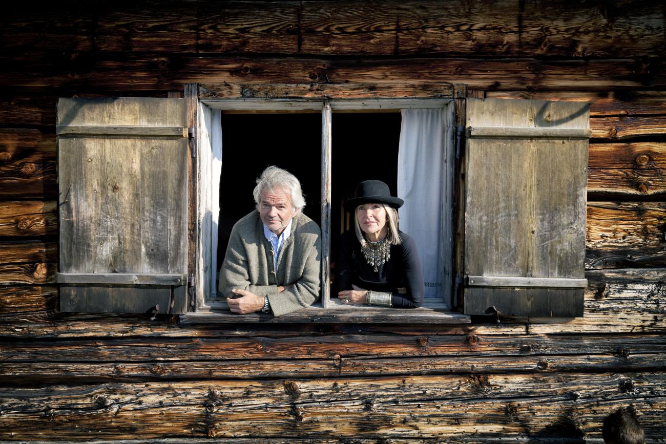 Ein Mann und eine Frau, die durch ein Fenster einer alten Holzhütte schauen