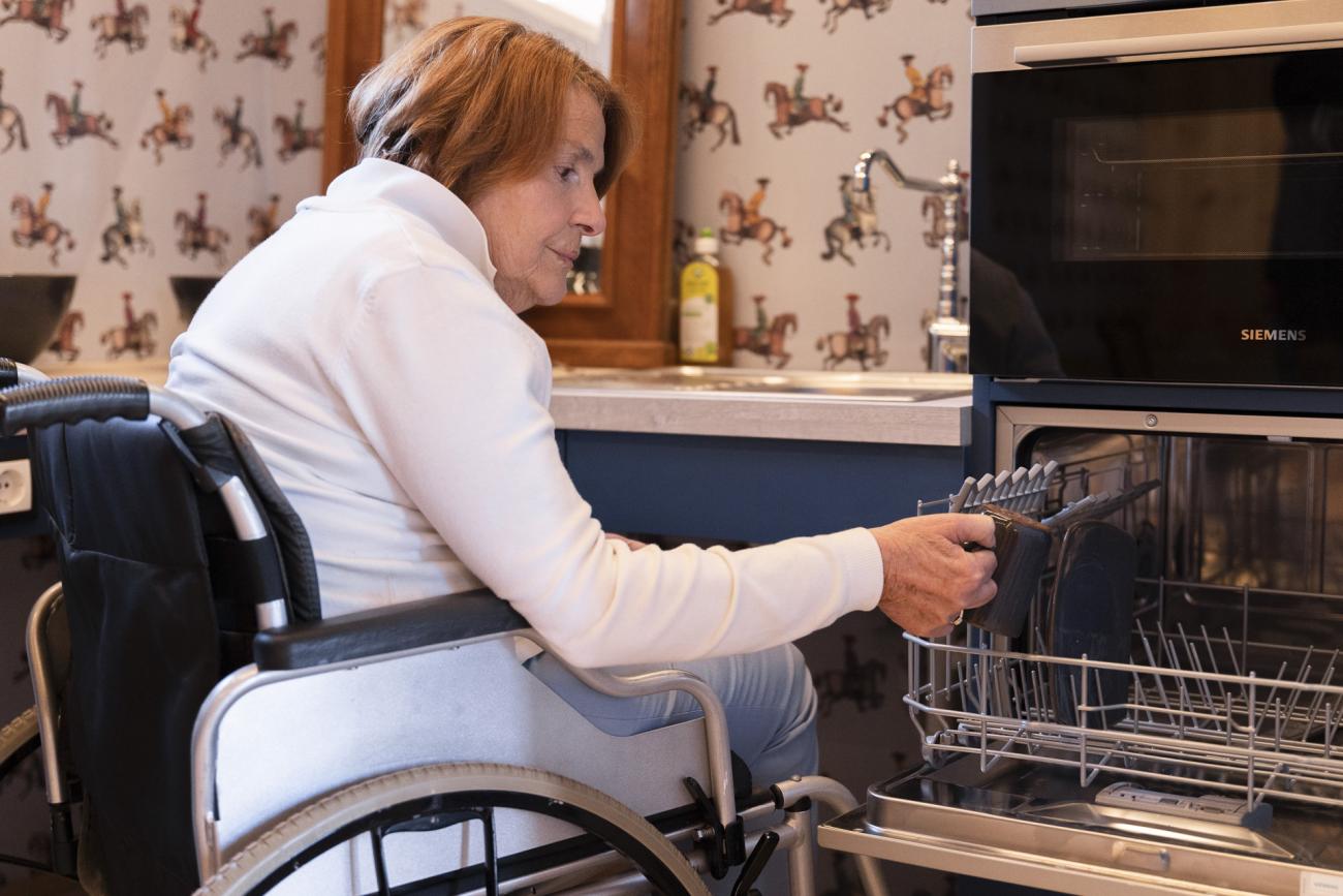 Frau im Rollstuhl, die einen Geschirrspüler einräumt