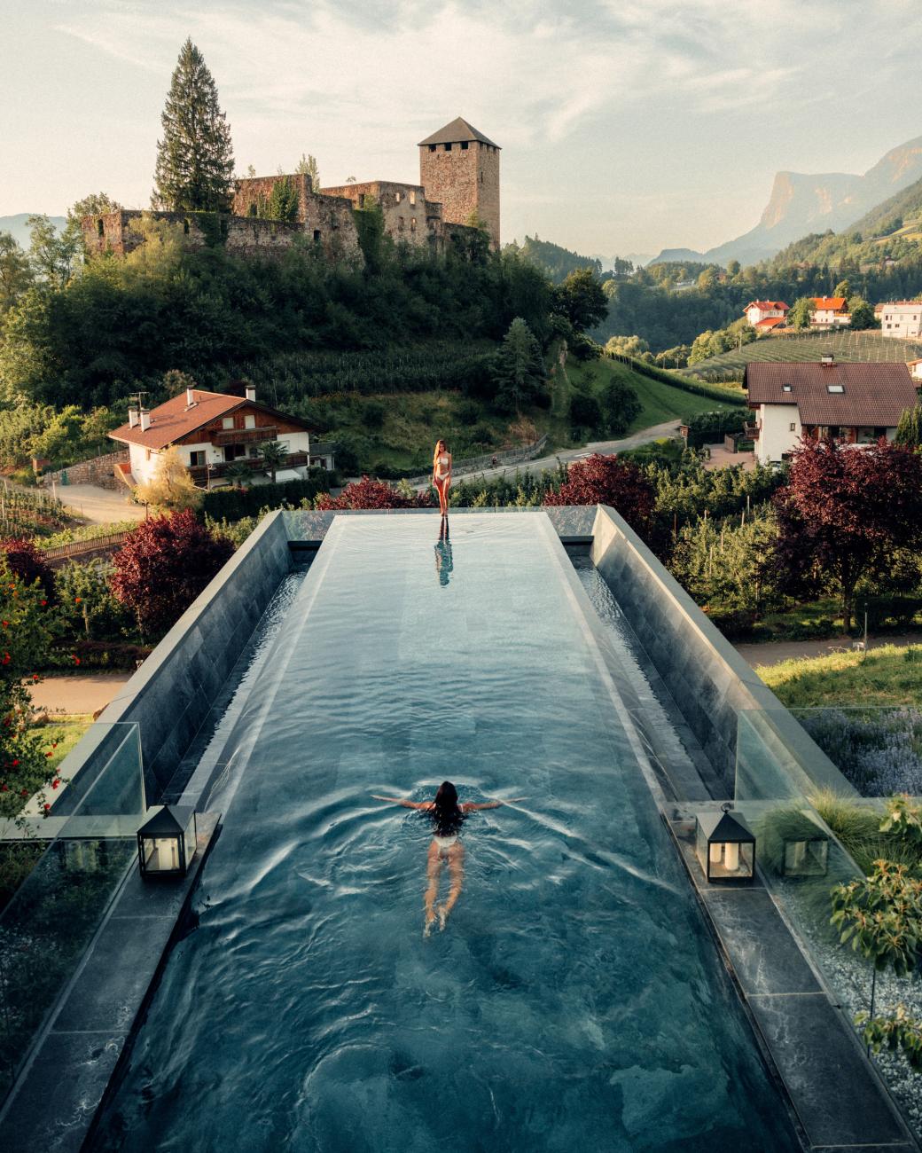 Langer Pool, in dem eine Frau schwimmt mit Blick auf eine Burg