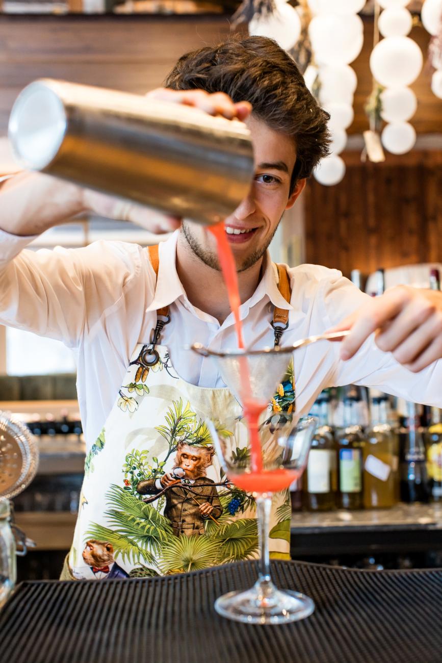 Barkeeper schüttet rotes Getränk in ein Cocktailglas