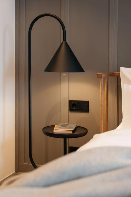 Eine schwarze moderne Stehlampe, die neben einem Bett steht