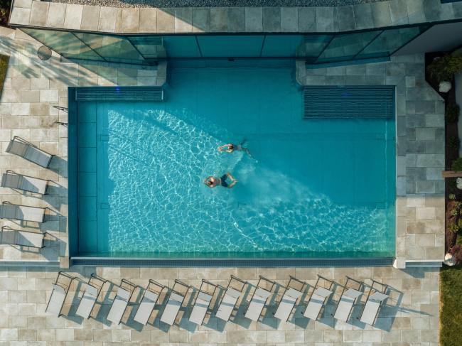Drohnenbild eines Pools mit Liegen und einem Pärchen, das im Wasser schimmt