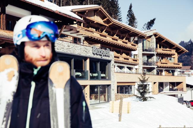 Mann in Skiausrüstung vor einem Holzhaus