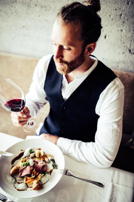 Sitzender Mann mit einem Glas Rotwein in der Hand und einem Teller auf dem Tisch