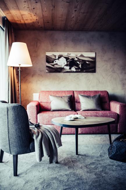 Wohnzimmer mit roter Couch, Holztisch, einer Lampe und grauem Teppich
