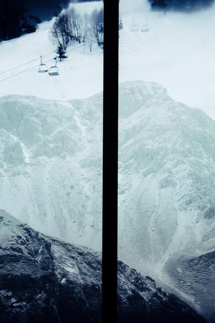Fenster mit Ausblick auf einen verschneiten Gipfel und Gondeln