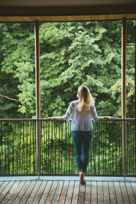 Frau, die auf einem Balkon steht und auf grüne Bäume schaut