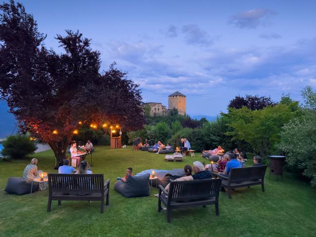 Menschen, die auf einer Wiese in der Abendstimmung sitzen und bei einem Konzert zuschauen