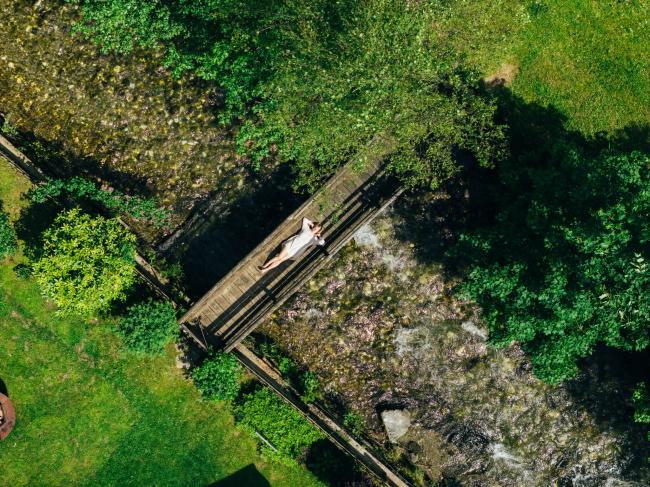Frau liegt im Grünen auf einer Brücke, die über einen Bach führt