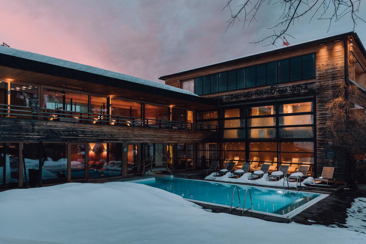 Naturhotel Chesa Valisa: Holzhaus mit Pool in verschneiter Abenddämmerung